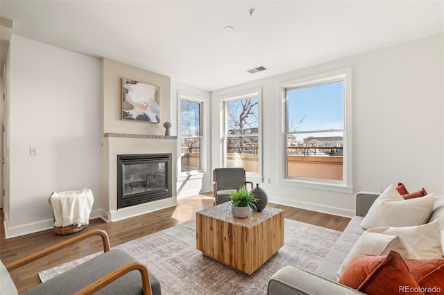 living room featuring baseboards, wood finished floors, visible vents, and a glass covered fireplace