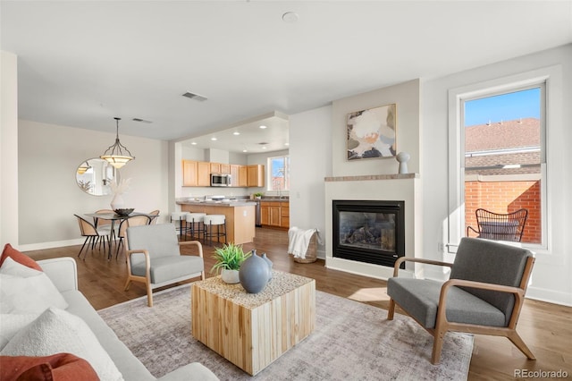 living area with a glass covered fireplace, light wood-style flooring, plenty of natural light, and visible vents