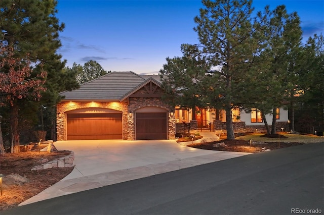 view of front of home with an attached garage, stone siding, driveway, and a tiled roof