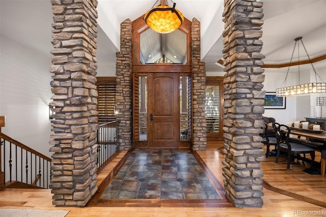 entryway featuring a high ceiling, an inviting chandelier, wood finished floors, and ornate columns