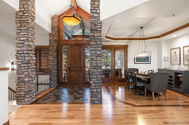 foyer featuring a raised ceiling, wood finished floors, decorative columns, and an inviting chandelier