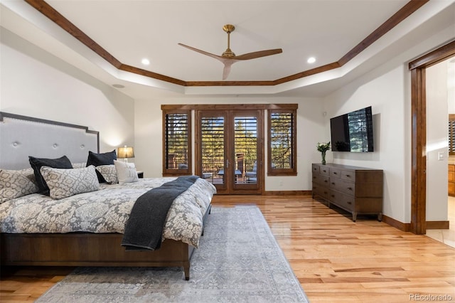 bedroom featuring a tray ceiling, light wood-style flooring, and baseboards