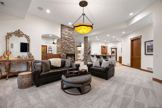 living area featuring arched walkways, a stone fireplace, baseboards, and light colored carpet