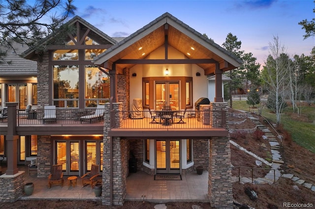 back of property at dusk with stucco siding, a patio, and french doors