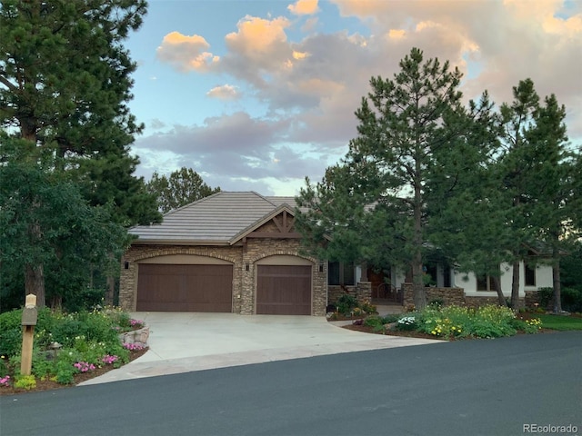 view of front facade with stone siding, an attached garage, concrete driveway, and a tile roof