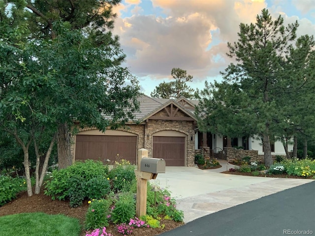 view of front of home with stone siding, an attached garage, driveway, and a tiled roof
