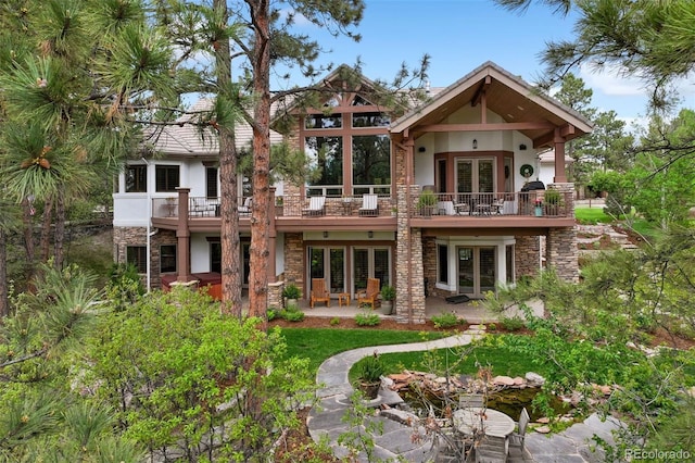 rear view of property with stucco siding, french doors, a balcony, stone siding, and a patio