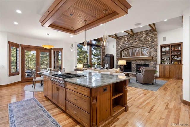 kitchen with stainless steel gas cooktop, a fireplace, open shelves, light wood-style flooring, and dark stone counters