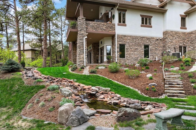 rear view of house featuring stone siding, a balcony, stucco siding, central AC, and stairs