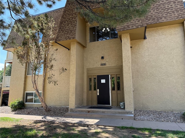 7695 E Quincy Ave Unit 207, Denver, CO 80237 - doorway to property with stucco siding, roof with shingles, and mansard roof