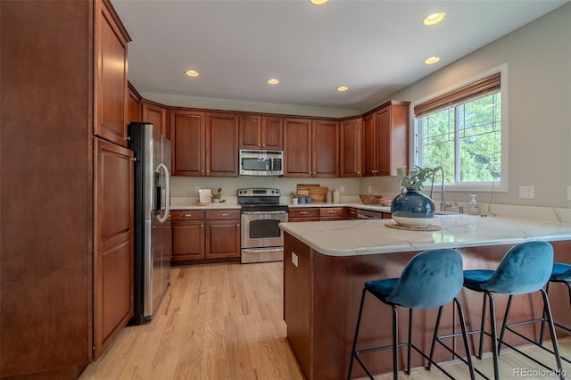 2908 Open Sky Way, Castle Rock, CO 80109 - kitchen featuring appliances with stainless steel finishes, a peninsula, light wood-type flooring, a kitchen breakfast bar, and recessed lighting