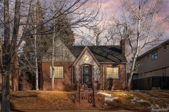 tudor-style house featuring brick siding, a chimney, and fence