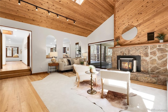 8782 S Ault Ln, Morrison, CO 80465 - living room featuring track lighting, wood finished floors, arched walkways, a stone fireplace, and baseboards