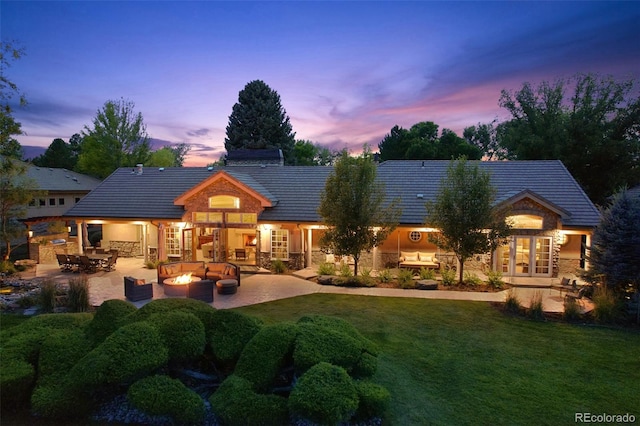 rear view of property featuring a patio, french doors, a lawn, and stone siding