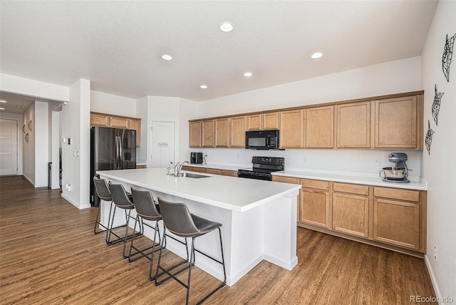 kitchen with a kitchen island with sink, dark wood-type flooring, sink, black appliances, and a breakfast bar area