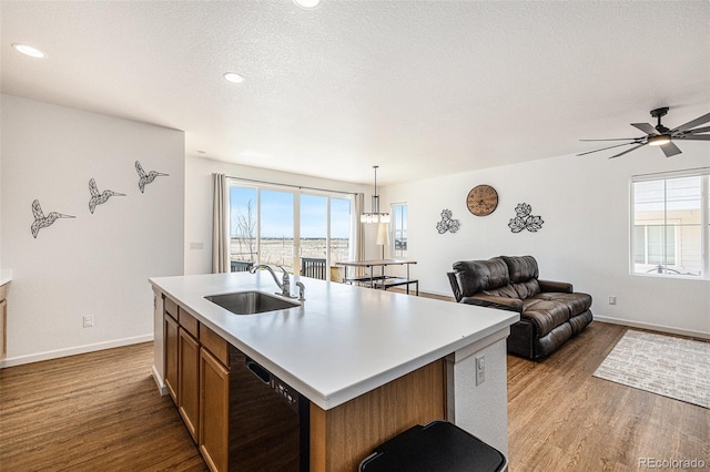 kitchen with sink, decorative light fixtures, a center island with sink, black dishwasher, and light hardwood / wood-style floors