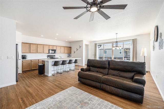 living room featuring recessed lighting, a textured ceiling, light wood-type flooring, baseboards, and ceiling fan with notable chandelier