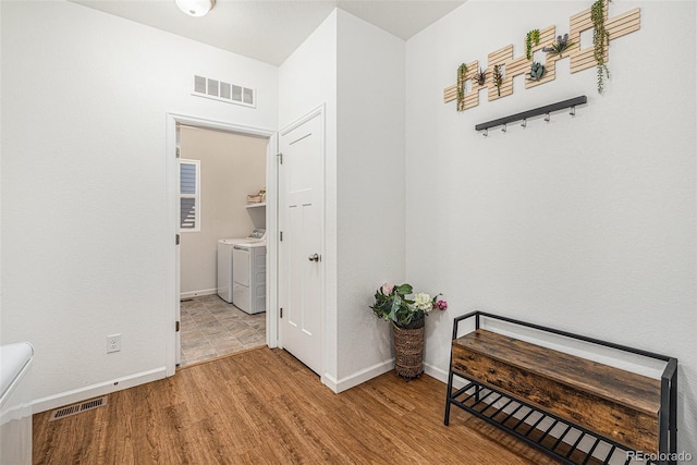 hallway featuring baseboards, washing machine and dryer, visible vents, and wood finished floors