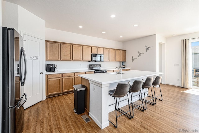 kitchen with black appliances, sink, an island with sink, light hardwood / wood-style floors, and a kitchen bar