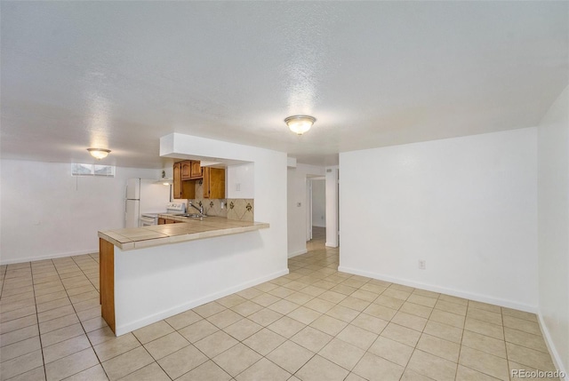 kitchen with sink, backsplash, a textured ceiling, kitchen peninsula, and white fridge