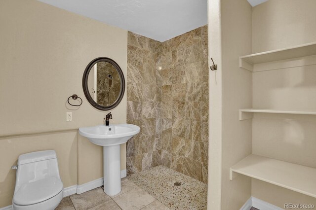 bathroom featuring toilet, a tile shower, and tile patterned flooring