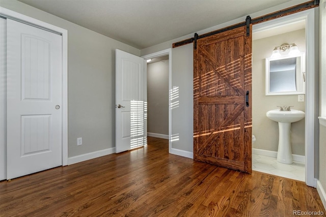 5500 Holland Dr, Arvada, CO 80002 - unfurnished bedroom with a barn door, wood finished floors, baseboards, a sink, and ensuite bath