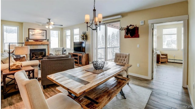 dining area featuring ceiling fan with notable chandelier, light wood-type flooring, baseboard heating, and a tiled fireplace