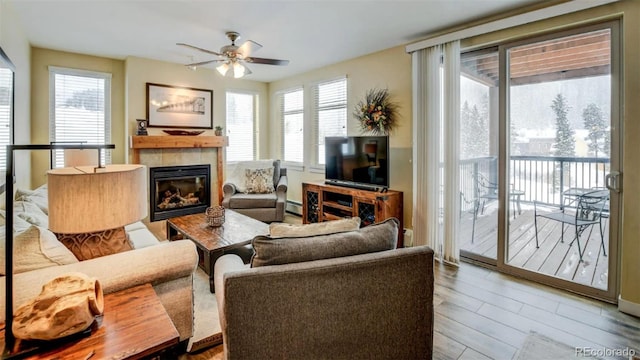 living room with baseboard heating, a tiled fireplace, ceiling fan, and wood-type flooring