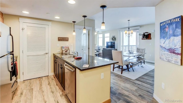 kitchen with light wood-type flooring, dark stone counters, sink, pendant lighting, and a chandelier