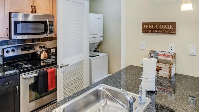 kitchen featuring sink, stainless steel appliances, tasteful backsplash, stacked washer / dryer, and dark stone countertops