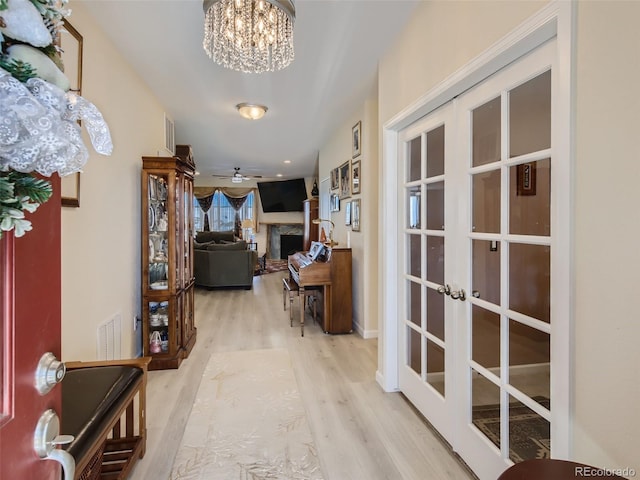 corridor featuring french doors, light hardwood / wood-style floors, and a notable chandelier