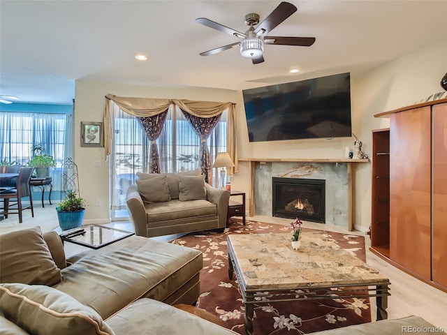 living room with a high end fireplace, light hardwood / wood-style floors, and ceiling fan