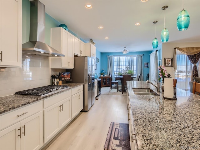 kitchen featuring white cabinetry, ceiling fan, wall chimney range hood, light stone counters, and decorative light fixtures