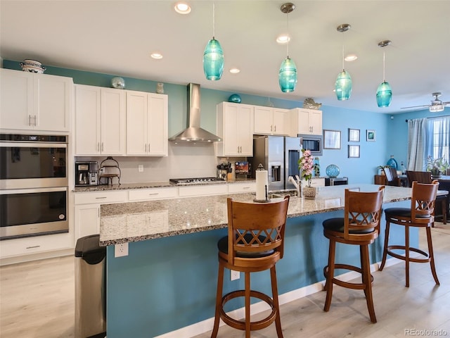 kitchen featuring white cabinetry, wall chimney range hood, hanging light fixtures, and stainless steel appliances