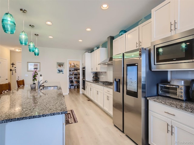 kitchen with sink, wall chimney range hood, a kitchen island with sink, white cabinets, and appliances with stainless steel finishes