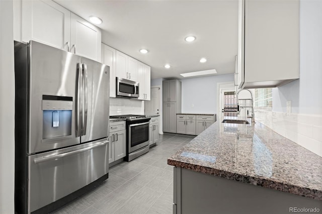 kitchen featuring backsplash, sink, light stone counters, white cabinetry, and stainless steel appliances