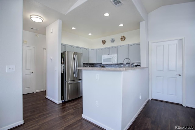 kitchen featuring sink, kitchen peninsula, backsplash, dark wood-type flooring, and stainless steel fridge