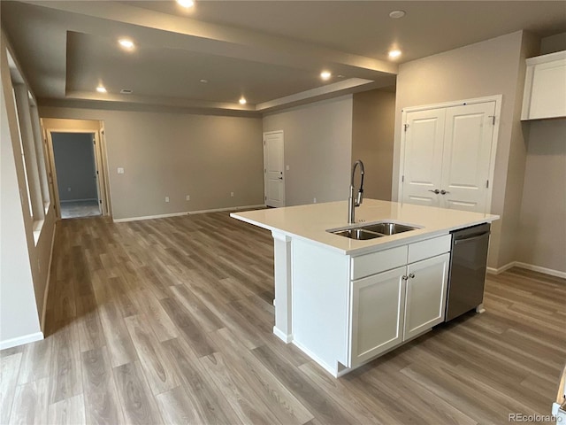 kitchen featuring a sink, dishwasher, a tray ceiling, baseboards, and light wood-style floors