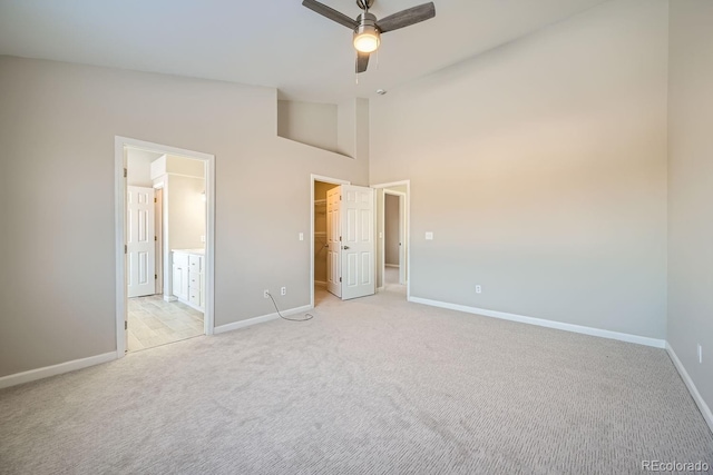 unfurnished bedroom featuring ceiling fan, high vaulted ceiling, light colored carpet, and ensuite bath