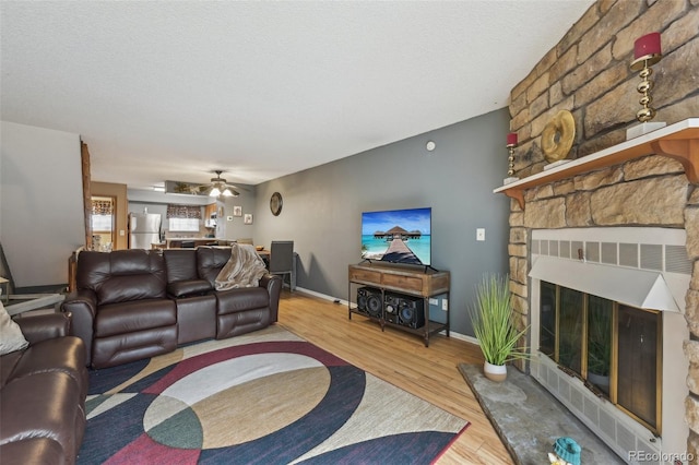 living area with a fireplace, ceiling fan, a textured ceiling, wood finished floors, and baseboards