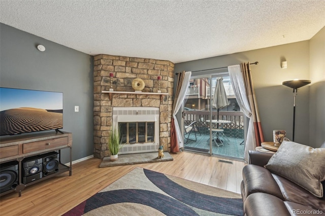 living room featuring a textured ceiling, a fireplace, visible vents, and wood finished floors