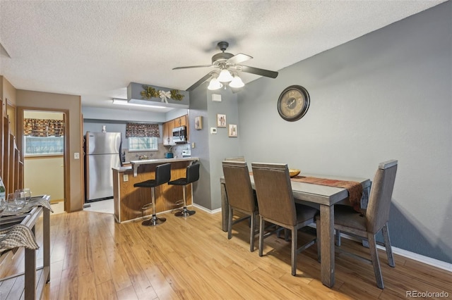 dining space featuring light wood-style floors, a textured ceiling, baseboards, and a ceiling fan