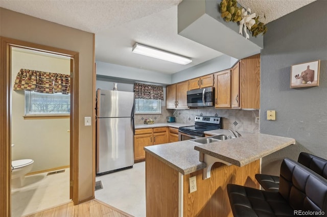 kitchen featuring a breakfast bar area, backsplash, a peninsula, stainless steel appliances, and a sink