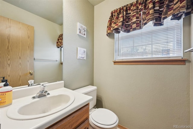 bathroom with a textured wall, vanity, and toilet