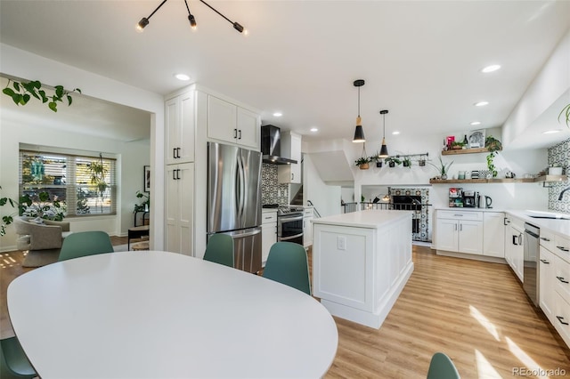 kitchen with appliances with stainless steel finishes, a kitchen island, wall chimney exhaust hood, pendant lighting, and white cabinets