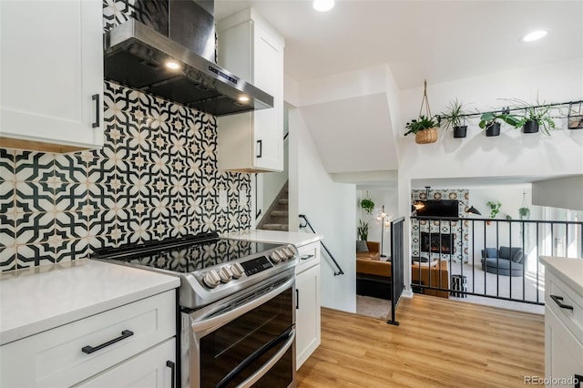 kitchen with wall chimney range hood, tasteful backsplash, white cabinetry, stainless steel electric range oven, and light hardwood / wood-style flooring