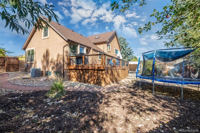 rear view of property featuring cooling unit, a deck, and a trampoline