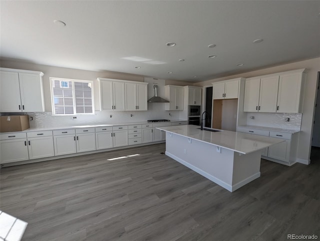 kitchen featuring white cabinets, hardwood / wood-style flooring, wall chimney exhaust hood, an island with sink, and gas cooktop