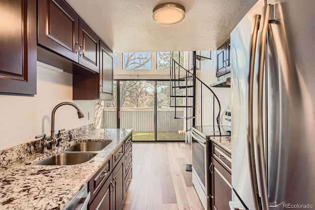 kitchen with a textured ceiling, under cabinet range hood, a sink, appliances with stainless steel finishes, and light wood-type flooring