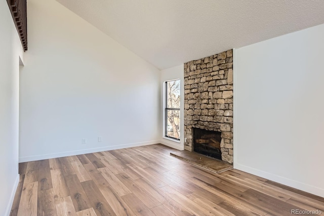 unfurnished living room with a textured ceiling, a fireplace, vaulted ceiling, and wood finished floors